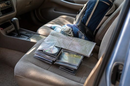 Stack of CDs in a family car with a road map and travel blanket, illustrating the best road trip CDs for families.