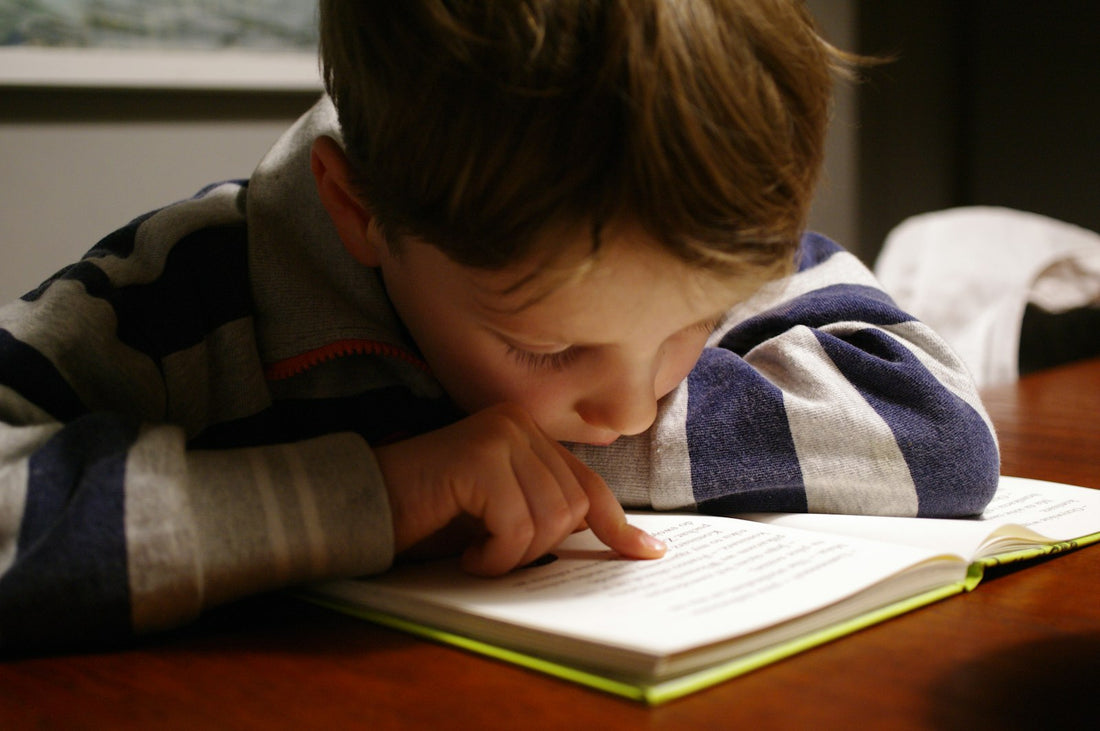 A child reading a book at a wooden table – Roald Dahl Books in Order